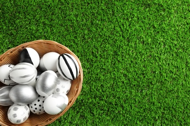 Photo of Wicker basket of painted Easter eggs on green lawn, top view with space for text