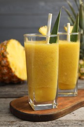 Photo of Tasty pineapple smoothie and cut fruit on wooden table