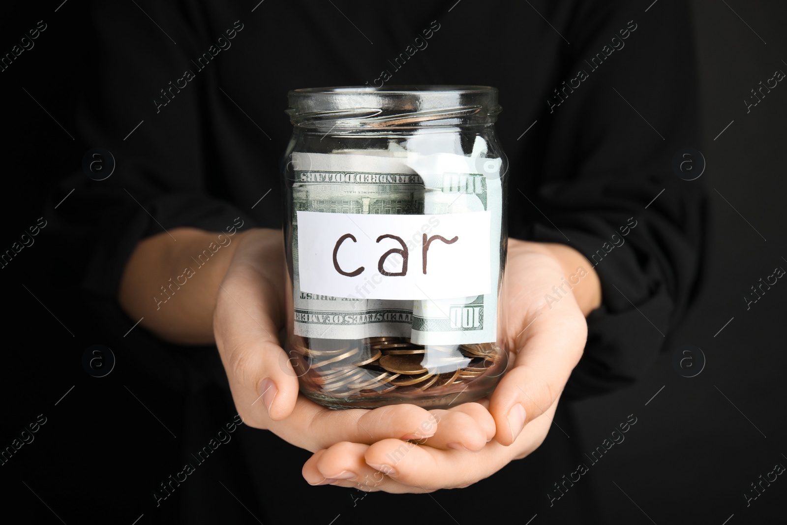 Photo of Woman holding glass jar with money and tag CAR on black background, closeup