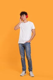 Photo of Handsome young man listening to music with headphones on orange background