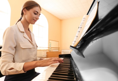 Photo of Young woman playing piano indoors. Music lesson