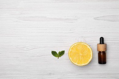 Bottle of citrus essential oil and fresh lemon on white wooden table, flat lay. Space for text