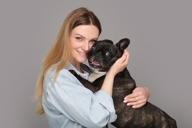 Photo of Portrait of happy woman hugging cute French Bulldog on grey background
