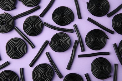 Tasty black liquorice candies on violet background, flat lay