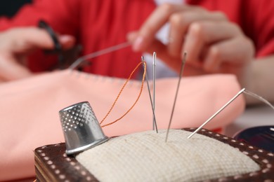 Photo of Woman cutting sewing thread over cloth, focus on pin cushion with needles and thimble