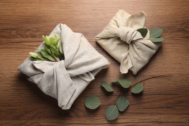 Photo of Furoshiki technique. Gift packed in different fabrics decorated with plants on wooden table, flat lay