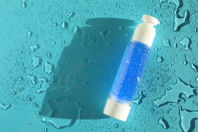 Photo of Bottle of cosmetic product on wet turquoise background, top view. Space for text