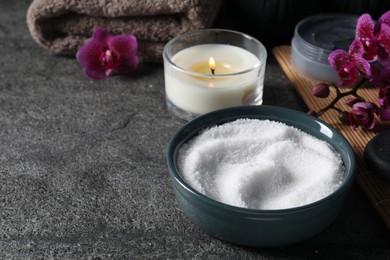 Beautiful composition with sea salt, burning candle, flowers and different spa products on grey table, space for text