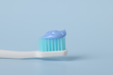 Photo of Plastic toothbrush with paste on light blue background, closeup