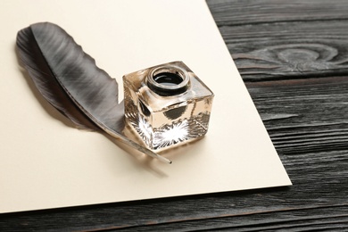 Feather pen, inkwell and blank parchment on wooden table