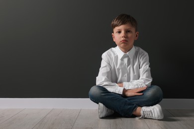 Photo of Little boy sitting on floor near black wall, space for text. School bullying