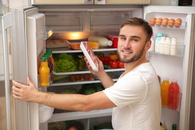 Photo of Young man taking meat from refrigerator in kitchen