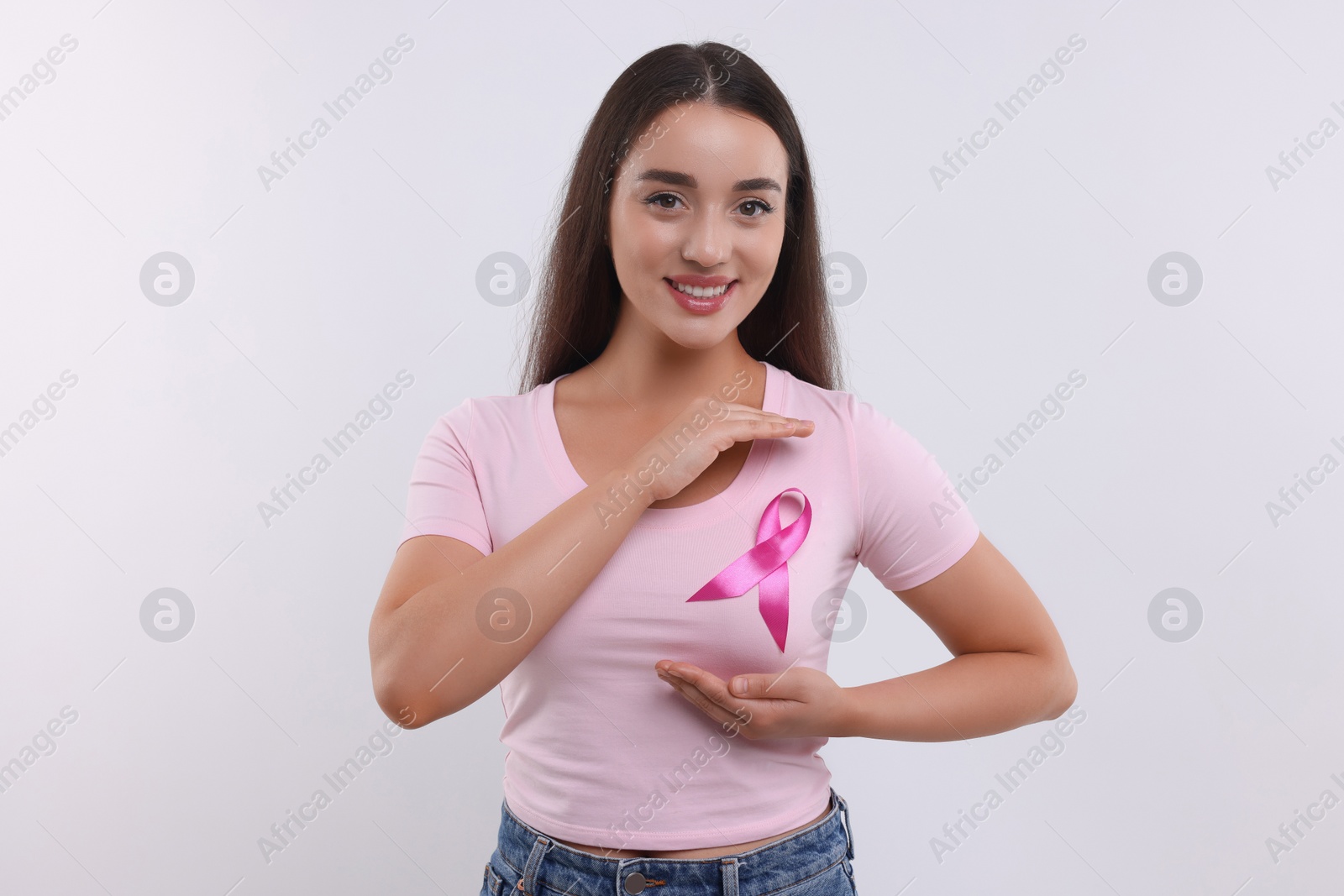 Photo of Beautiful young woman with pink ribbon on white background. Breast cancer awareness