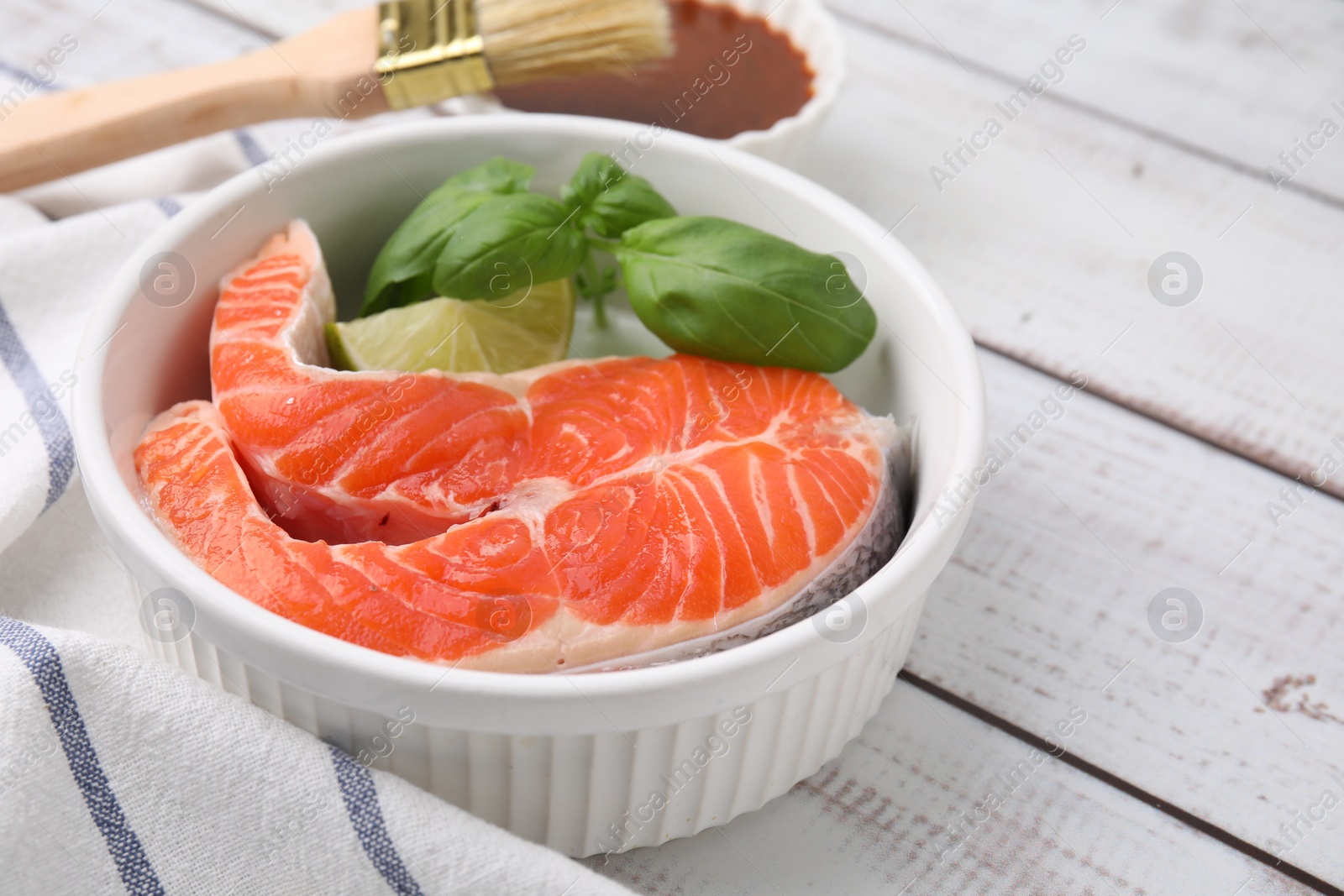 Photo of Fresh marinated fish, brush and lime on white wooden table, closeup