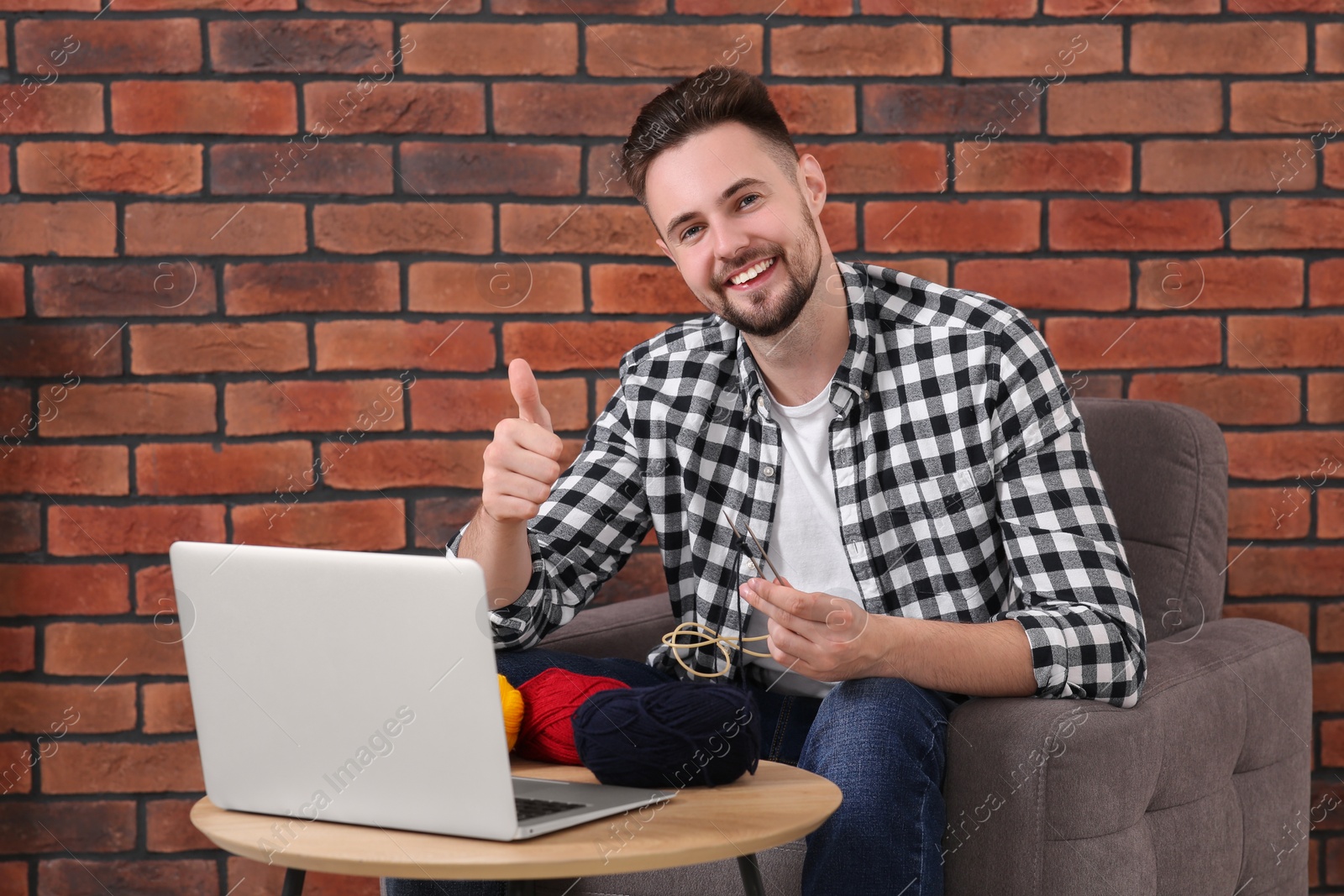 Photo of Happy man learning to knit with online course and showing thumb up at home. Time for hobby