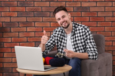 Photo of Happy man learning to knit with online course and showing thumb up at home. Time for hobby