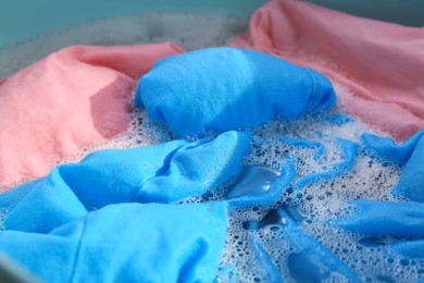 Photo of Colorful clothes in suds, closeup. Hand washing laundry