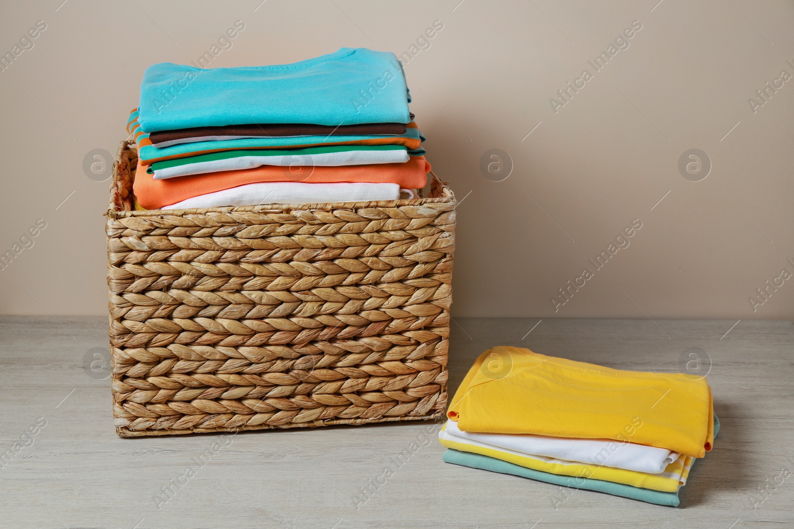 Photo of Wicker laundry basket with clean clothes on floor near beige wall