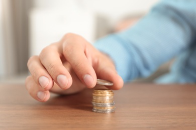 Photo of Closeup view of man stacking coins at table, focus on hand