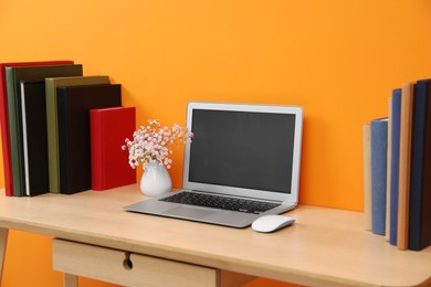 Photo of Hardcover books and laptop on wooden table near orange wall
