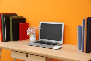 Hardcover books and laptop on wooden table near orange wall