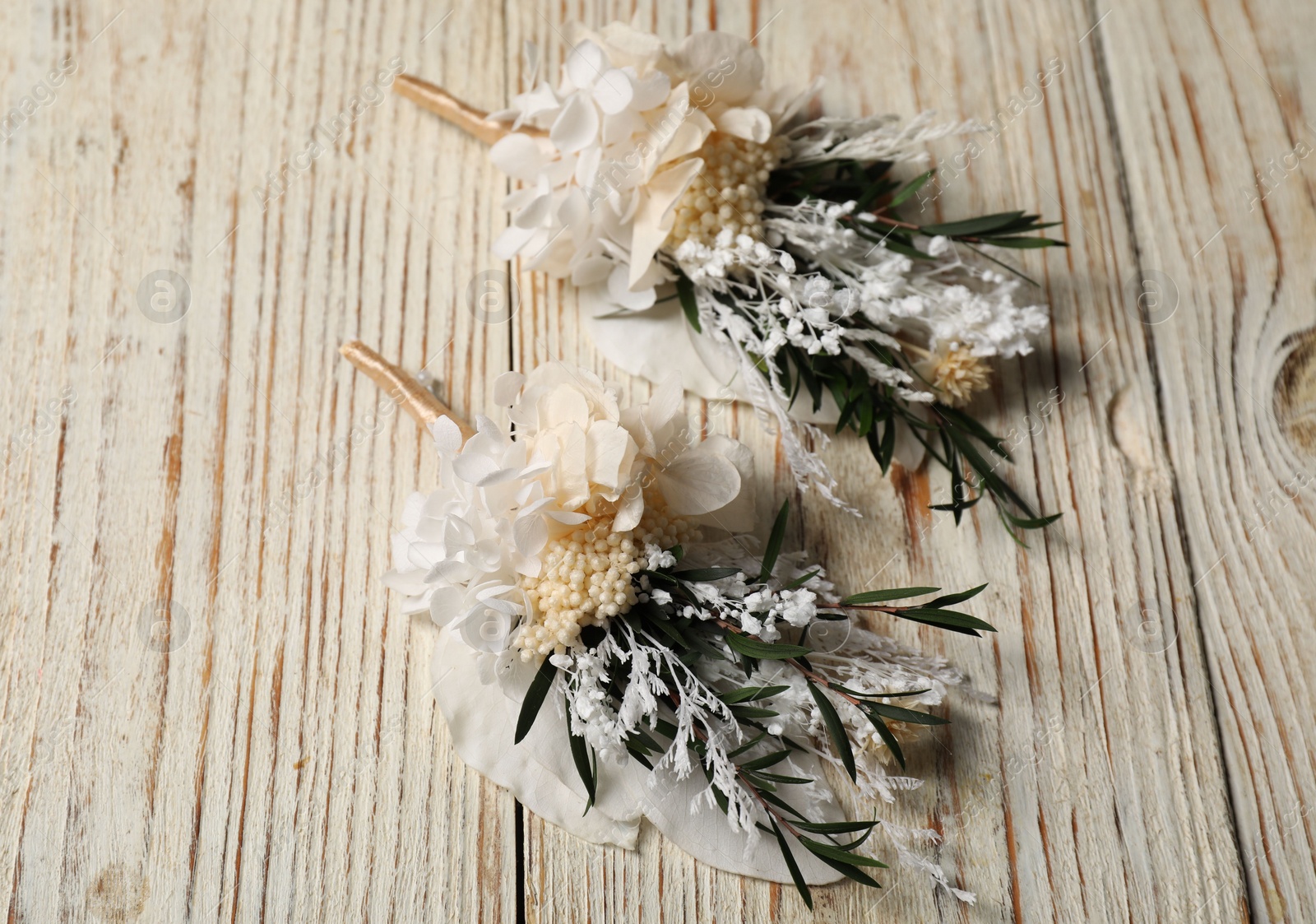 Photo of Stylish boutonnieres on light wooden table, above view