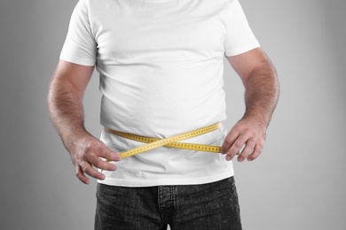 Photo of Fat man with measuring tape on grey background, closeup. Weight loss