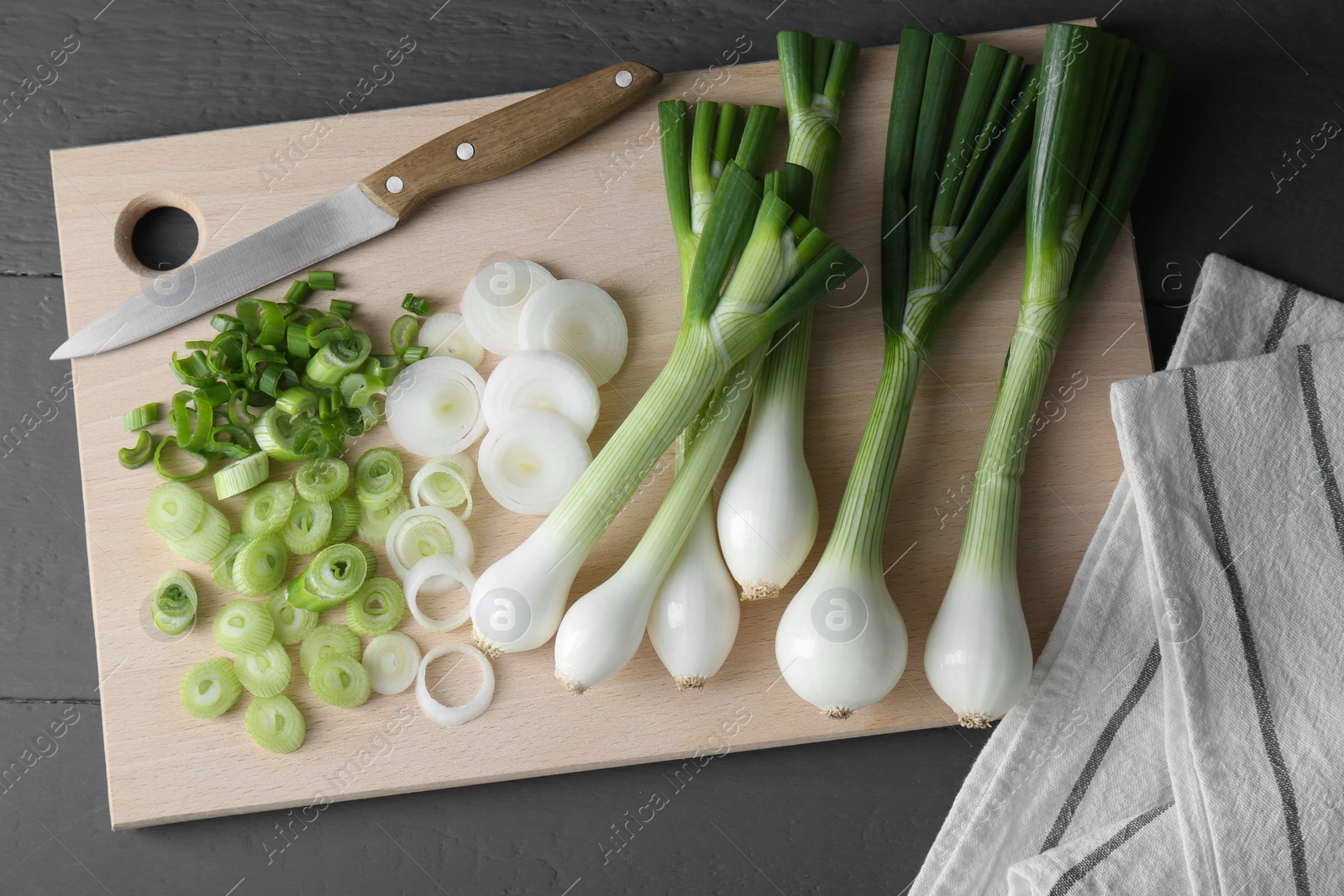 Photo of Board with knife, whole and cut spring onions on grey wooden table, flat lay