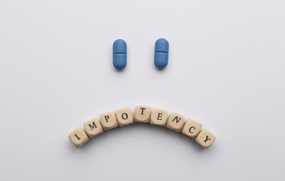 Photo of Sad face made of pills and cubes with word Impotency on white background, flat lay