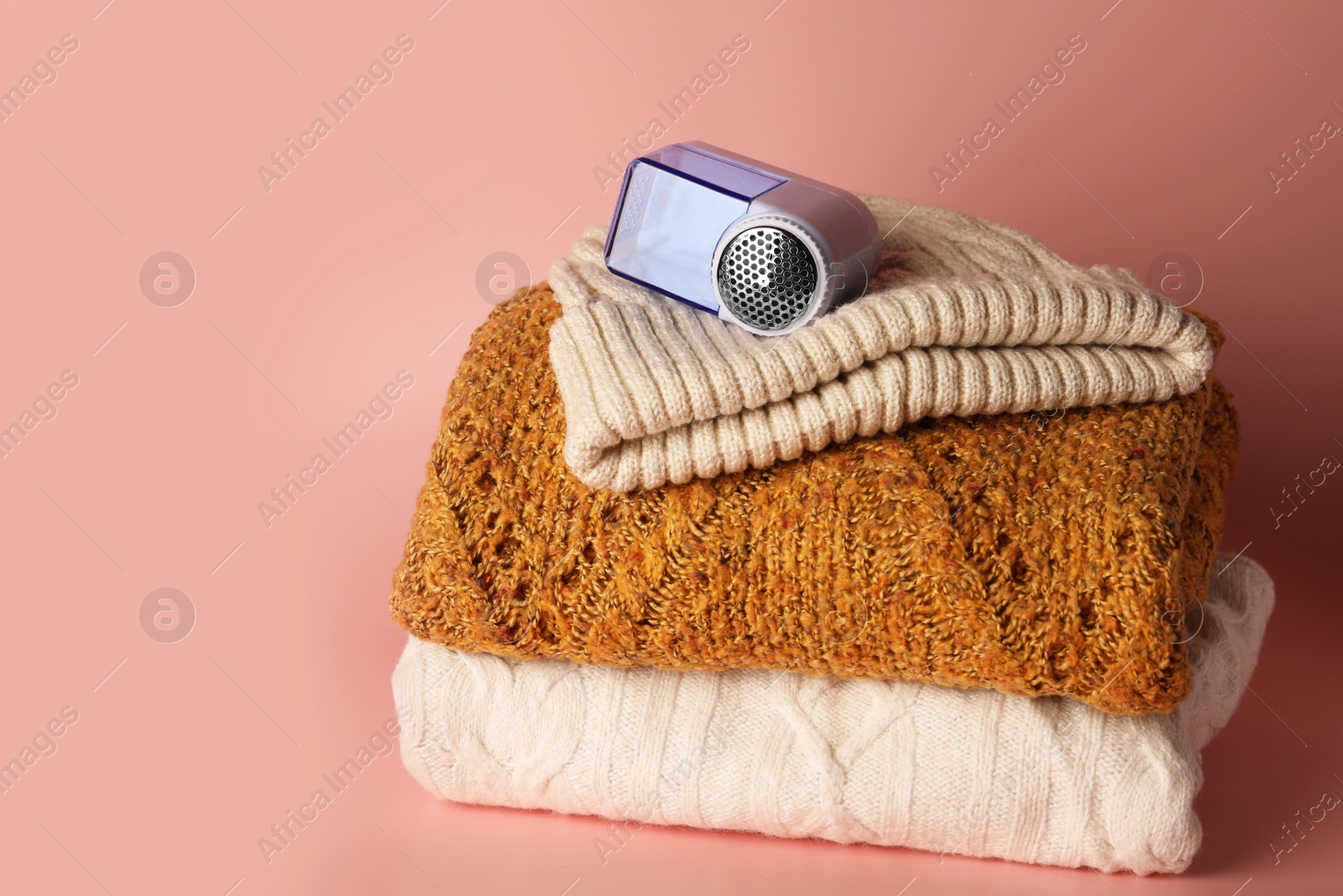Photo of Modern fabric shaver and knitted clothes on pink background, space for text