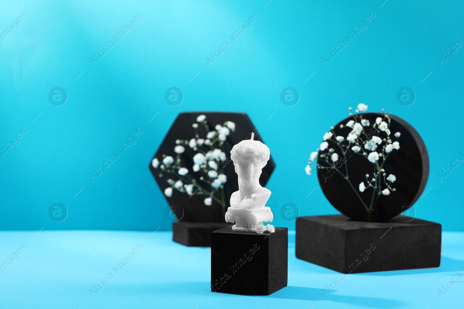 Photo of Stylish presentation of David bust candle and gypsophila flowers on light blue background. Space for text