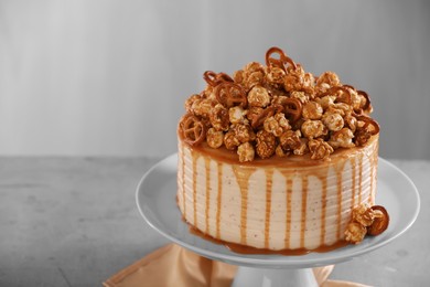 Caramel drip cake decorated with popcorn and pretzels on light grey table, space for text