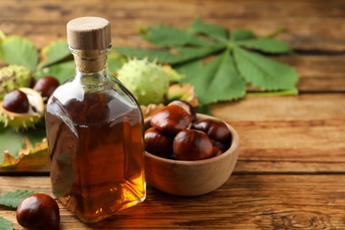 Photo of Chestnuts, leaves and bottle of essential oil on wooden table. Space for text