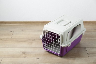Photo of Violet pet carrier on floor near white wall. Space for text