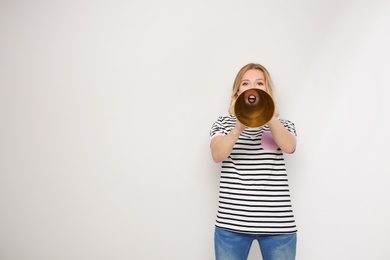 Photo of Young woman shouting into megaphone on light background. Space for text