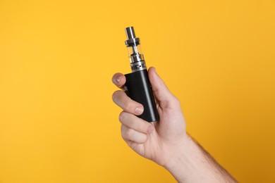 Photo of Man holding electronic cigarette on yellow background, closeup