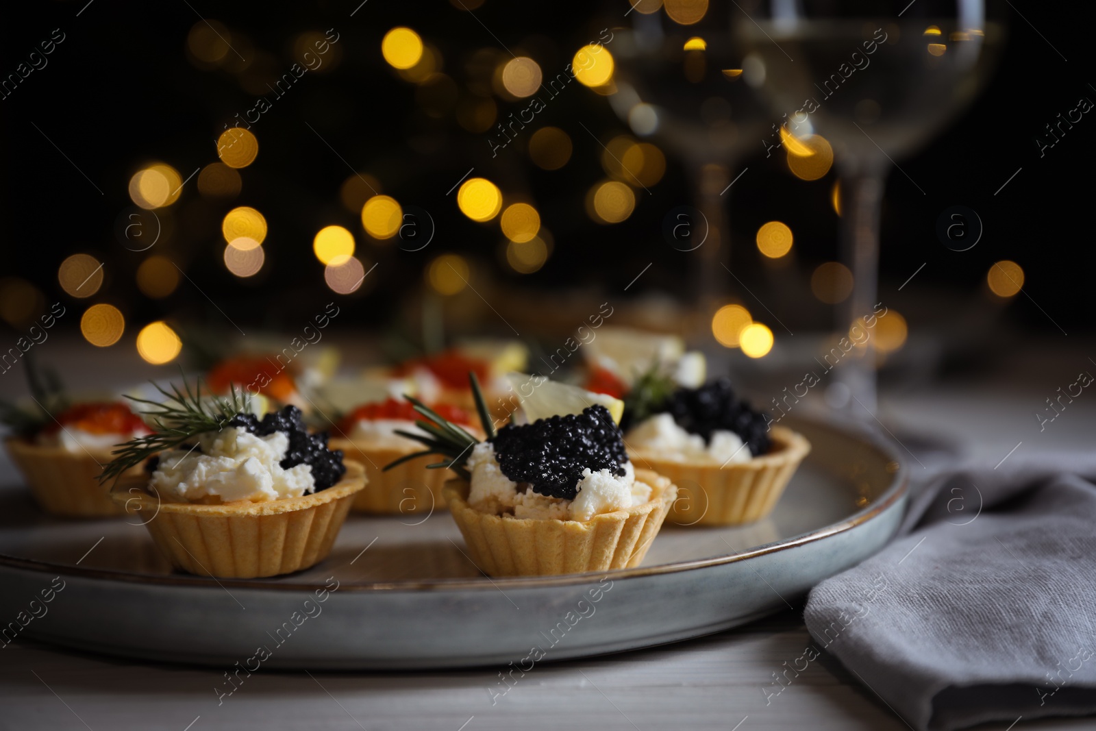 Photo of Delicious tartlets with red and black caviar served on white wooden table against blurred festive lights, closeup. Space for text