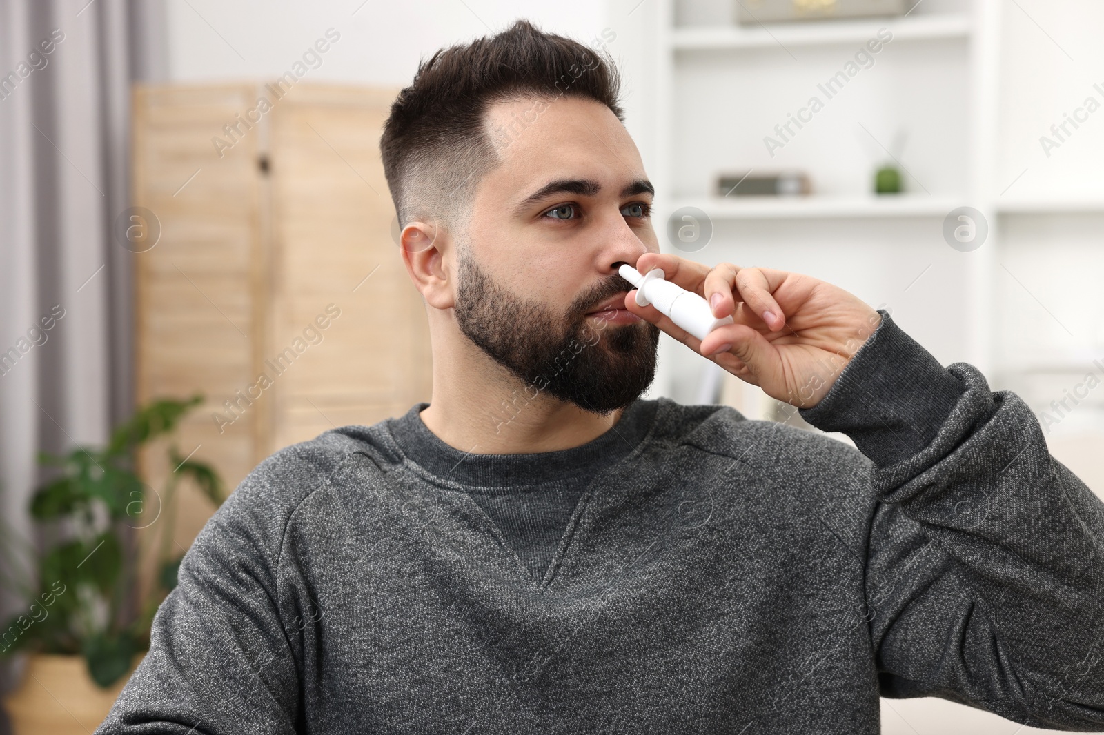 Photo of Medical drops. Young man using nasal spray indoors