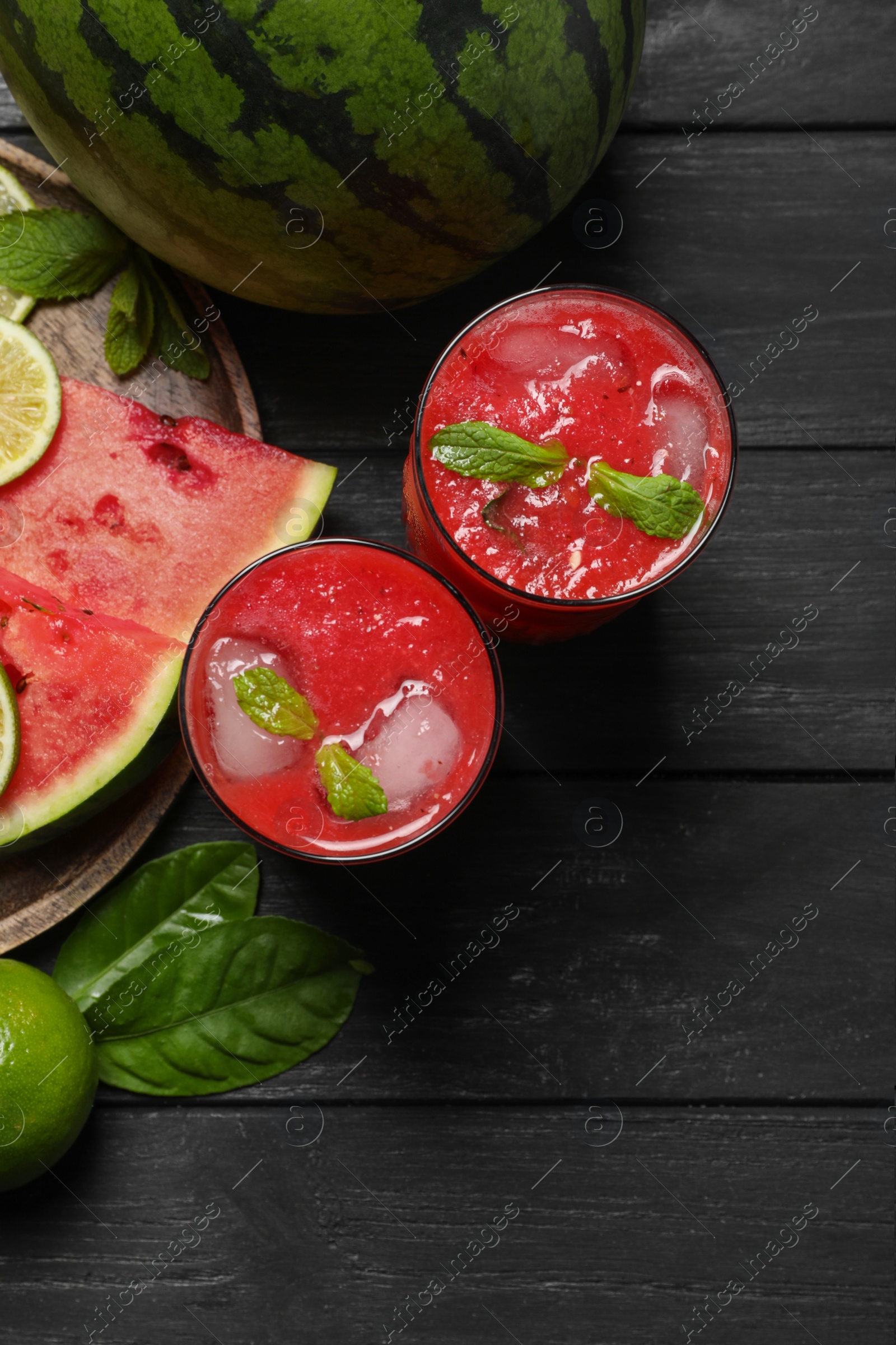 Photo of Glasses of delicious fresh watermelon juice, lime, mint and ice on black wooden table, flat lay. Space for text