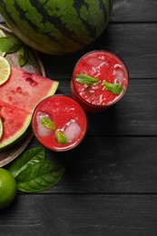 Photo of Glasses of delicious fresh watermelon juice, lime, mint and ice on black wooden table, flat lay. Space for text