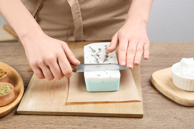 Woman cutting natural handmade soap on wooden table, closeup