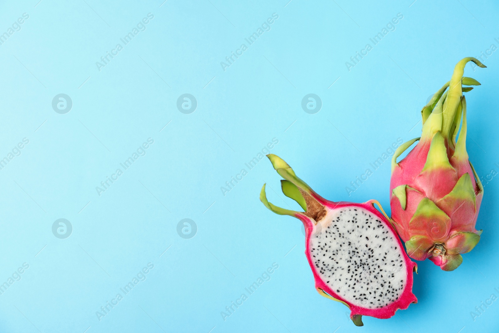 Photo of Delicious cut and whole dragon fruits (pitahaya) on light blue background, flat lay. Space for text