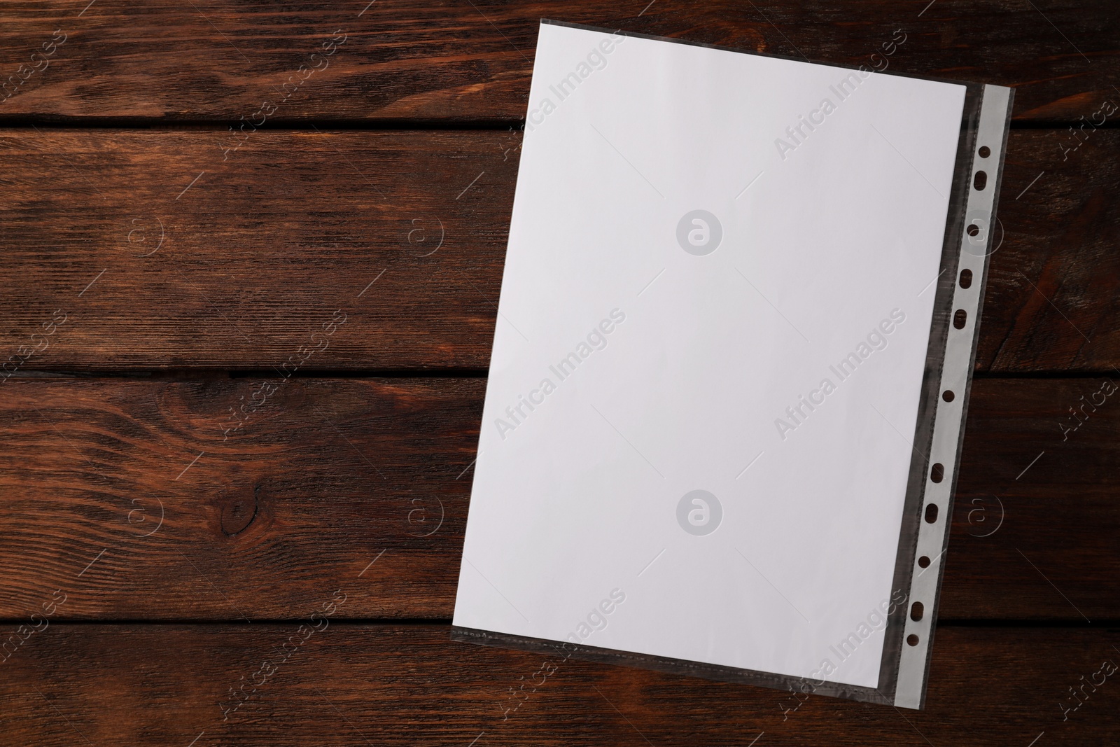 Photo of Punched pocket with paper sheet on wooden table, top view. Space for text