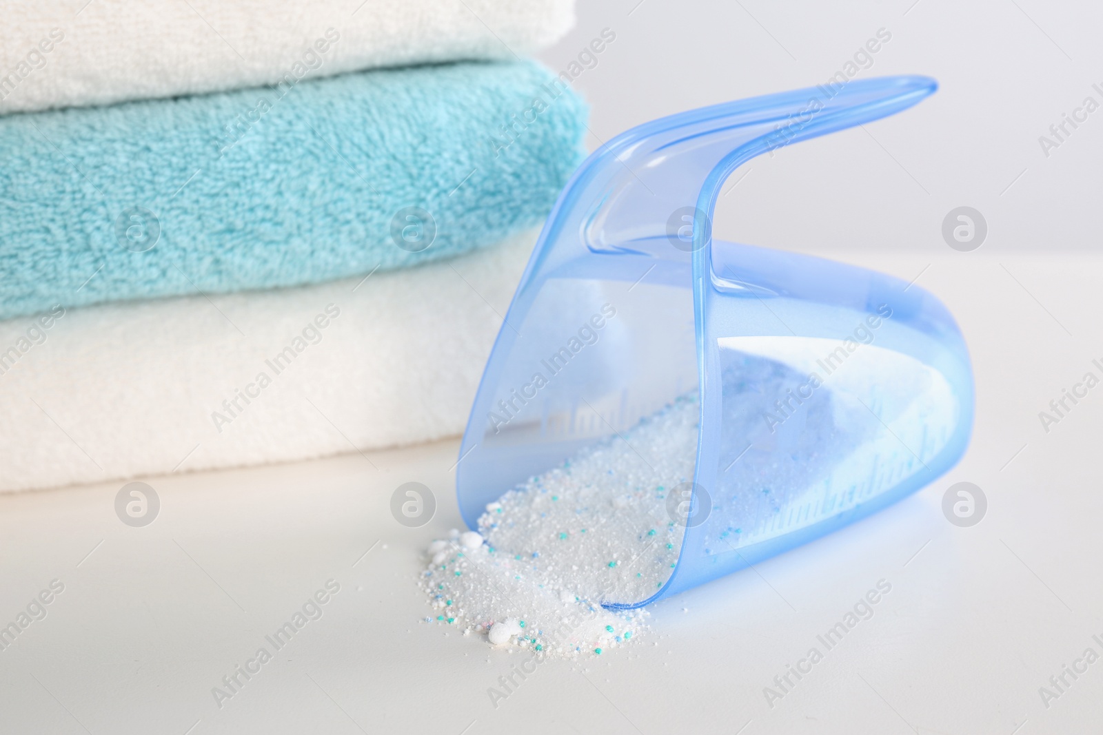 Photo of Measuring cup with washing powder and clean towels on white background. Laundry day