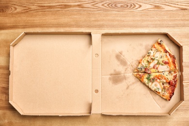 Photo of Cardboard box with pizza pieces on wooden background, top view
