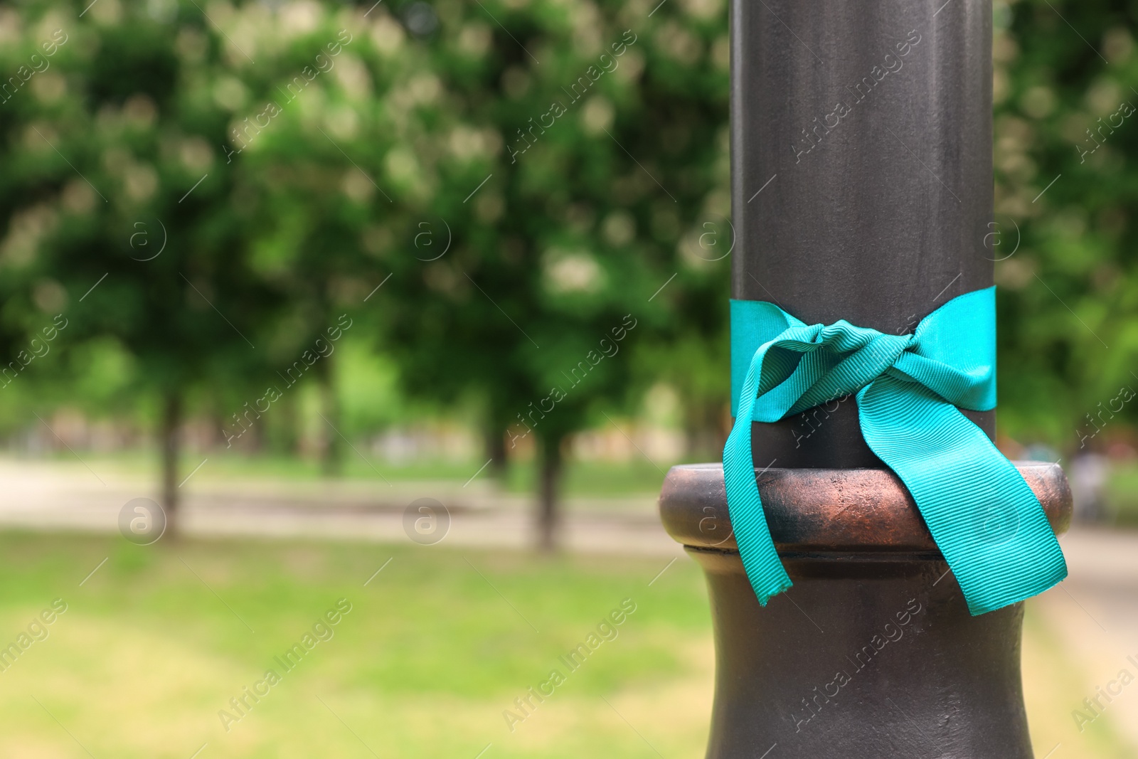 Photo of Teal awareness ribbon tied on lamppost in park, space for text