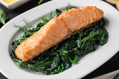 Photo of Tasty salmon with spinach on table, closeup