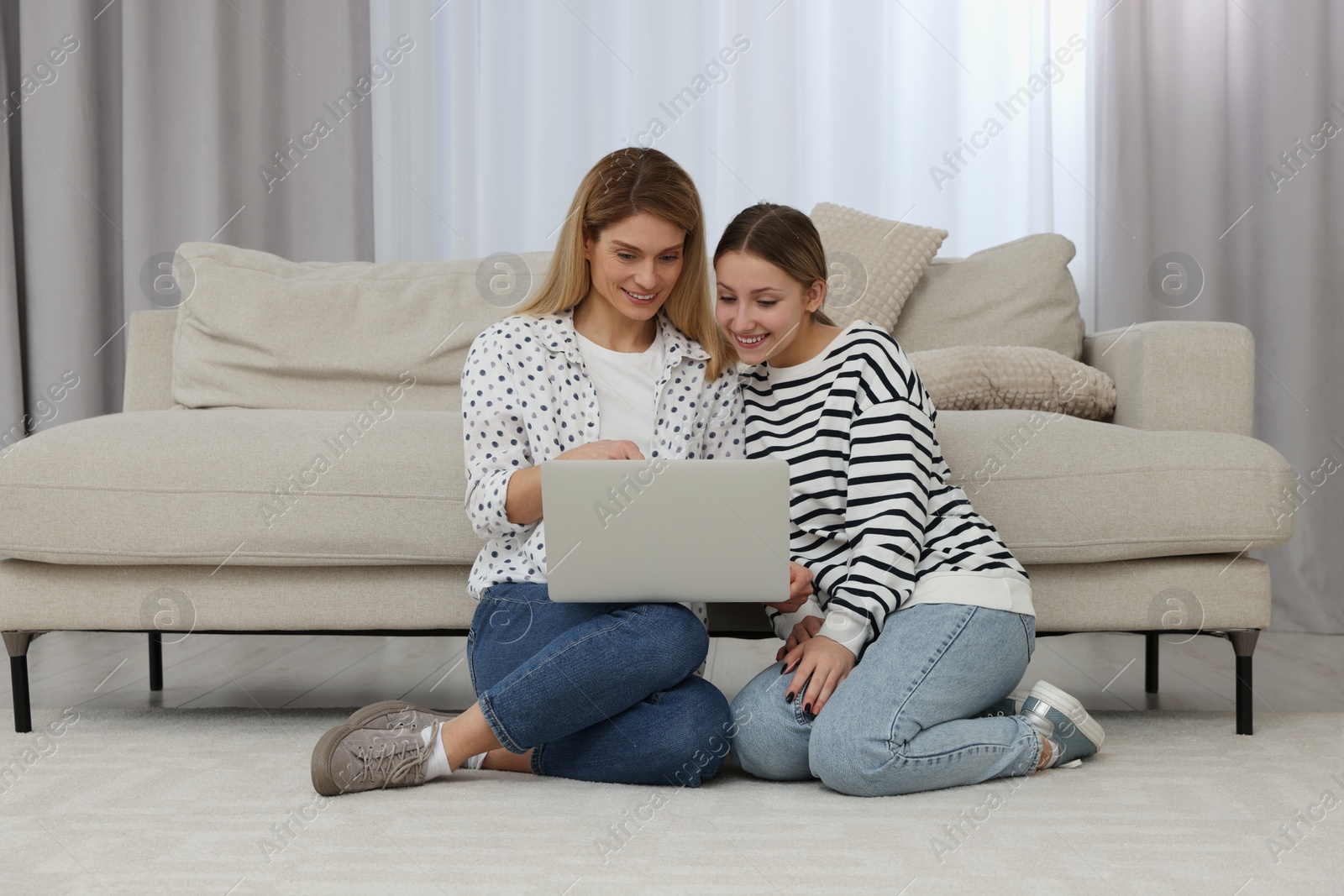 Photo of Happy mother and her teenage daughter with laptop on floor at home