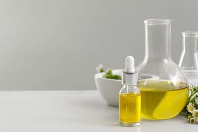 Photo of Bottle and flask of cosmetic oil on white table, space for text