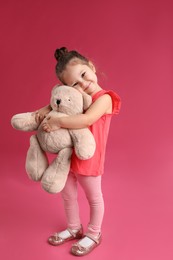 Cute little girl with teddy bear on pink background